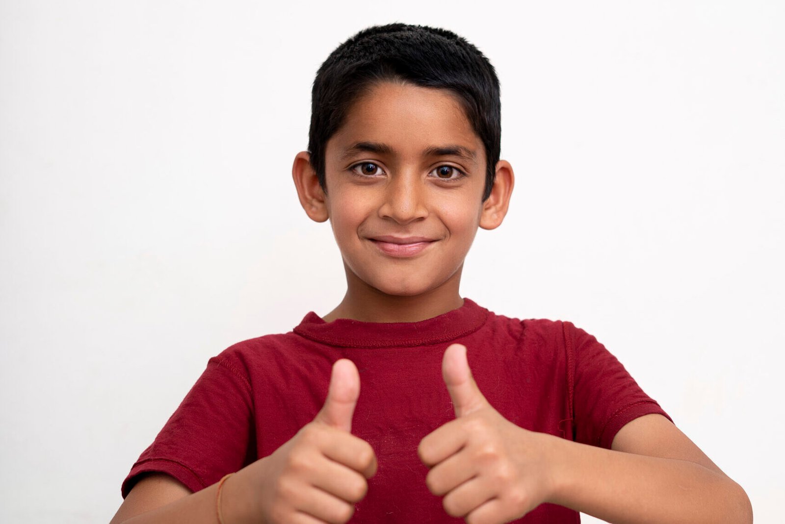young indian kid showing thumbs up into the camera while smiling. small kid education concept.